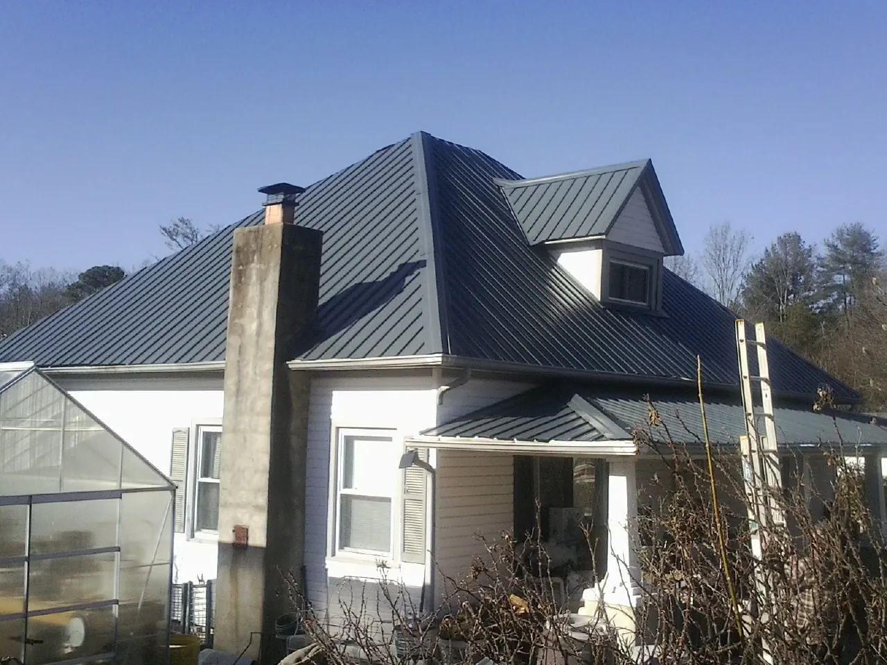 Dark blue standing seam metal roof on a white farmhouse with dormer — Slate & Tile Roof Repair by Roofing Brothers in Larimore