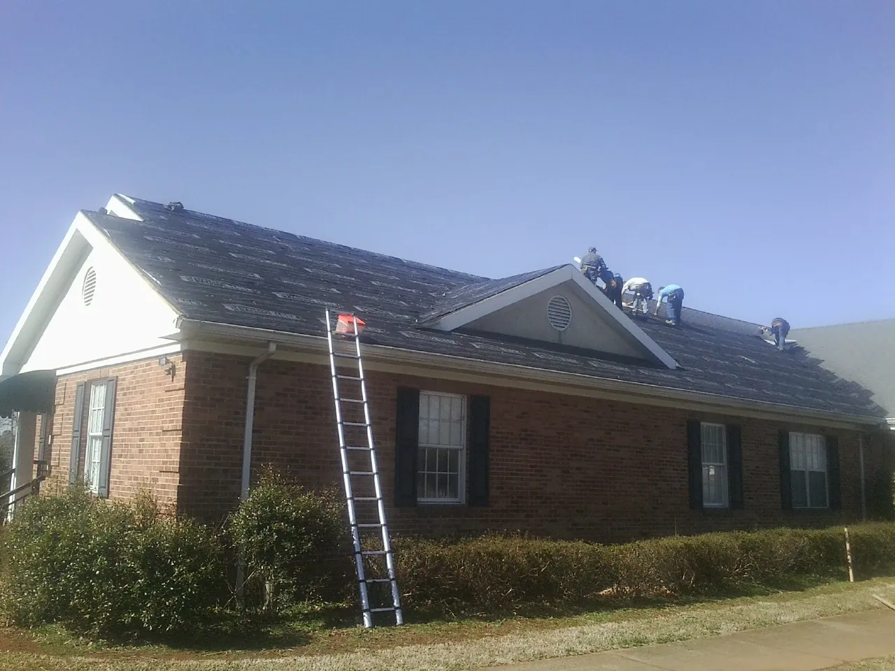 Crew tearing shingles off a brick ranch roof with a ladder set — Metal Roof Repair work by our crew in Larimore