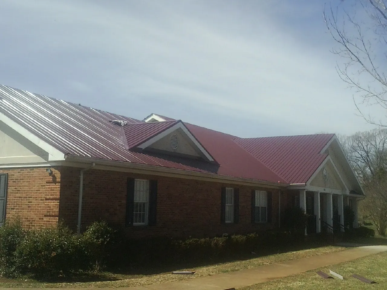 Red metal roof with gabled entries on a long brick building, from a Hail Damage Roof Repair job in Larimore