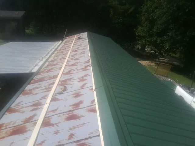 Old rusted panels beside newly installed green metal roofing — Wind Damage Roof Repair by Roofing Brothers in Larimore