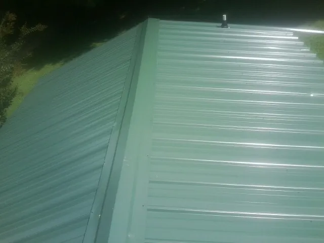 New green metal panels meeting at the ridge of a roof — Flat Roof Repair work by our crew in Larimore