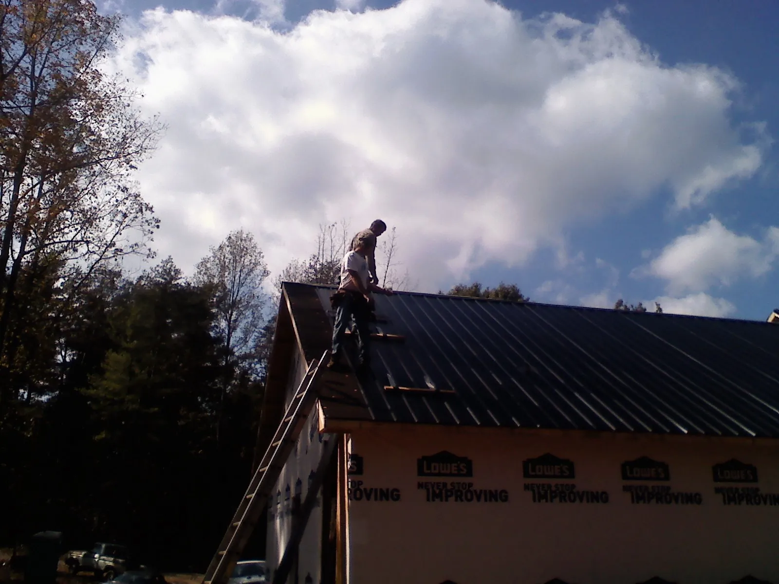 Roofer fastening dark metal panels high against a cloudy sky, from a Roof Inspection job in Larimore