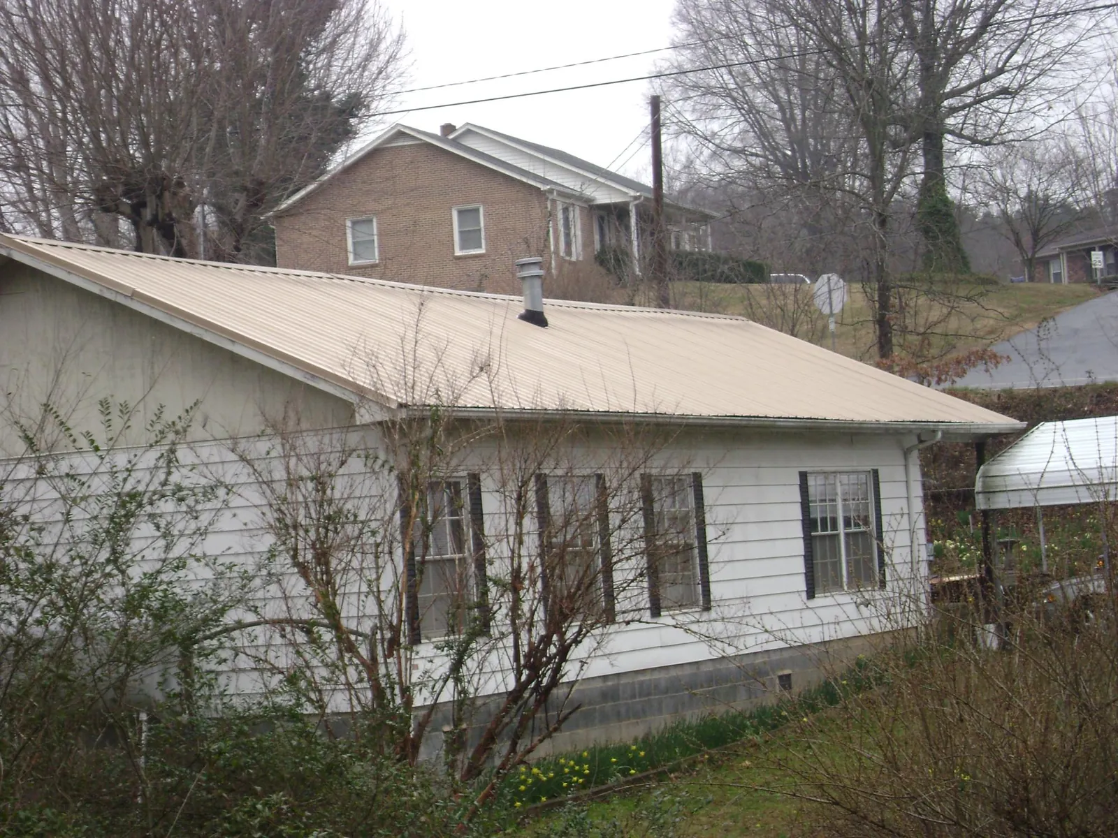 Tan metal roof on a white sided house set into a hillside — Commercial Roofing by Roofing Brothers in Larimore